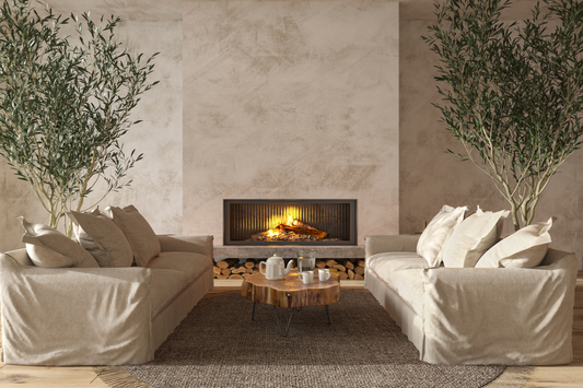Salón con chimenea encendida, sofás de lino enfrentados, olivos en maceta y mesa de centro de tronco de madera